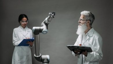 Dois pesquisadores de jaleco trabalham com um braço robótico em um laboratório.