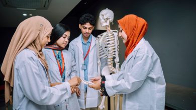 Grupo de estudantes de medicina reunido em uma sala de aula universitária ao redor de um esqueleto anatômico.