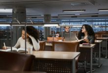 Estudantes universitários estudam com livros e laptops em uma biblioteca moderna.