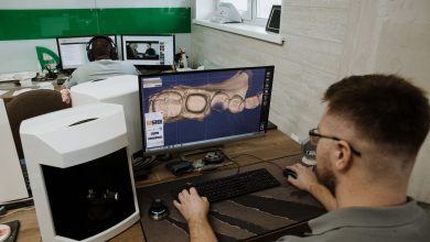 Profissional trabalha em um laboratório odontológico diante de um computador, criando um modelo digital de dentes.