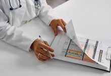 Profissional de saúde confere relatórios em uma prancheta dentro de um ambiente hospitalar.