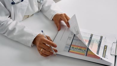 Profissional de saúde confere relatórios em uma prancheta dentro de um ambiente hospitalar.